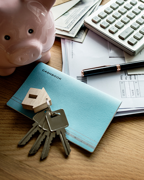 a wooden table with papers a cash book, calculator, piggy bank and keys to the house